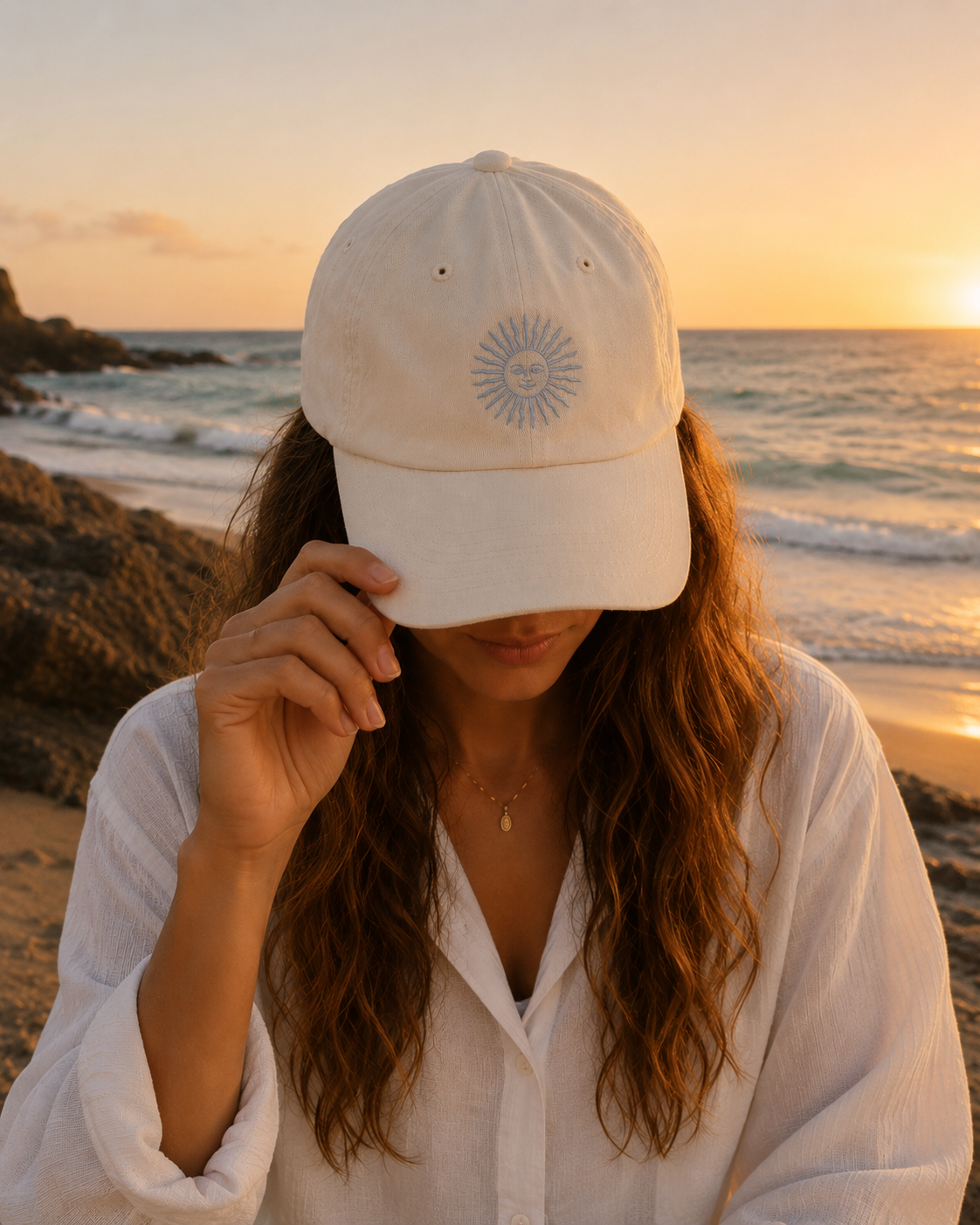 Person wearing a beige cap with a logo on a beach at sunset