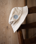The crema corduroy piluso resting on a rush-seat chair against a pale oak wall.